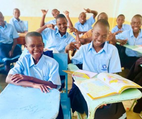 girls sitting at desks in blue school uniforms smiling at the camera